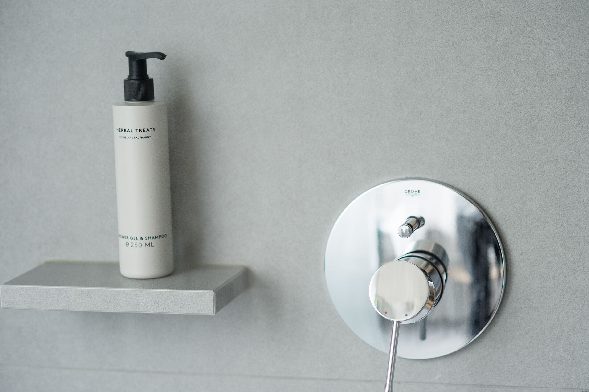 A bathroom with a white bottle of herbal treats and a modern faucet on a grey wall.