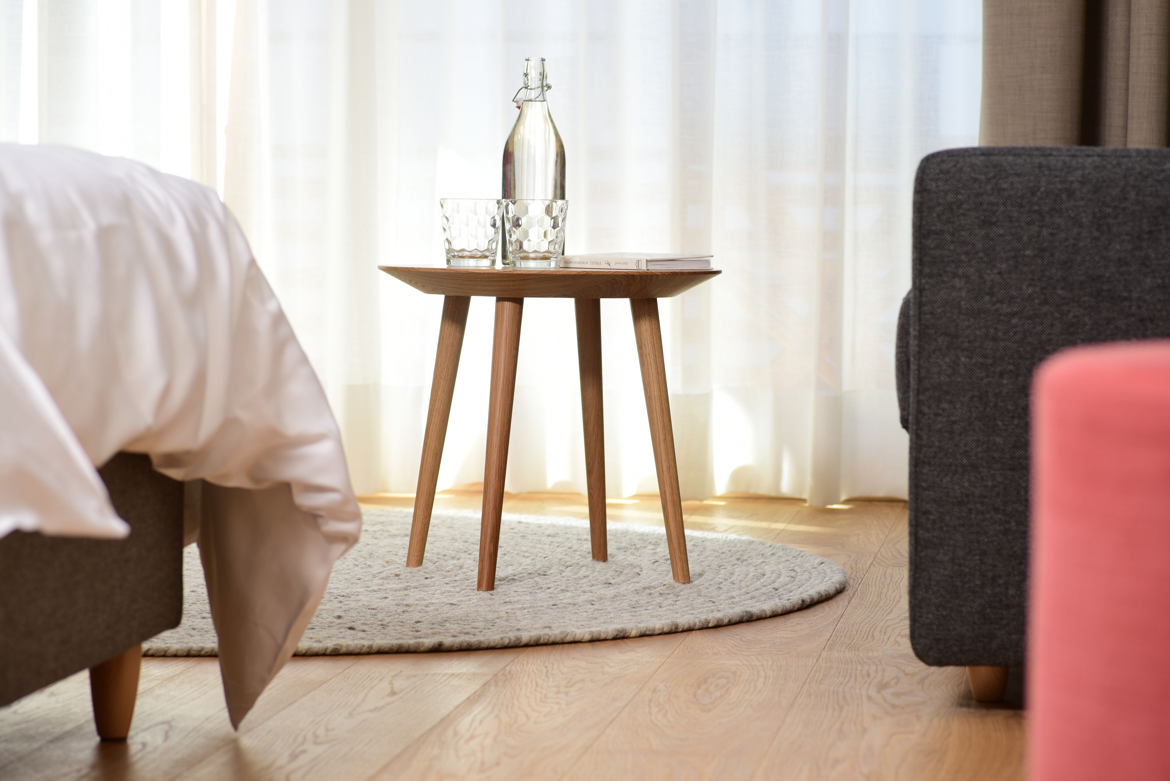 Ein ordentlich eingerichtetes Hotelzimmer mit einem Bett, einem kleinen runden Tisch mit Flasche und Gläsern sowie einem Stuhl.