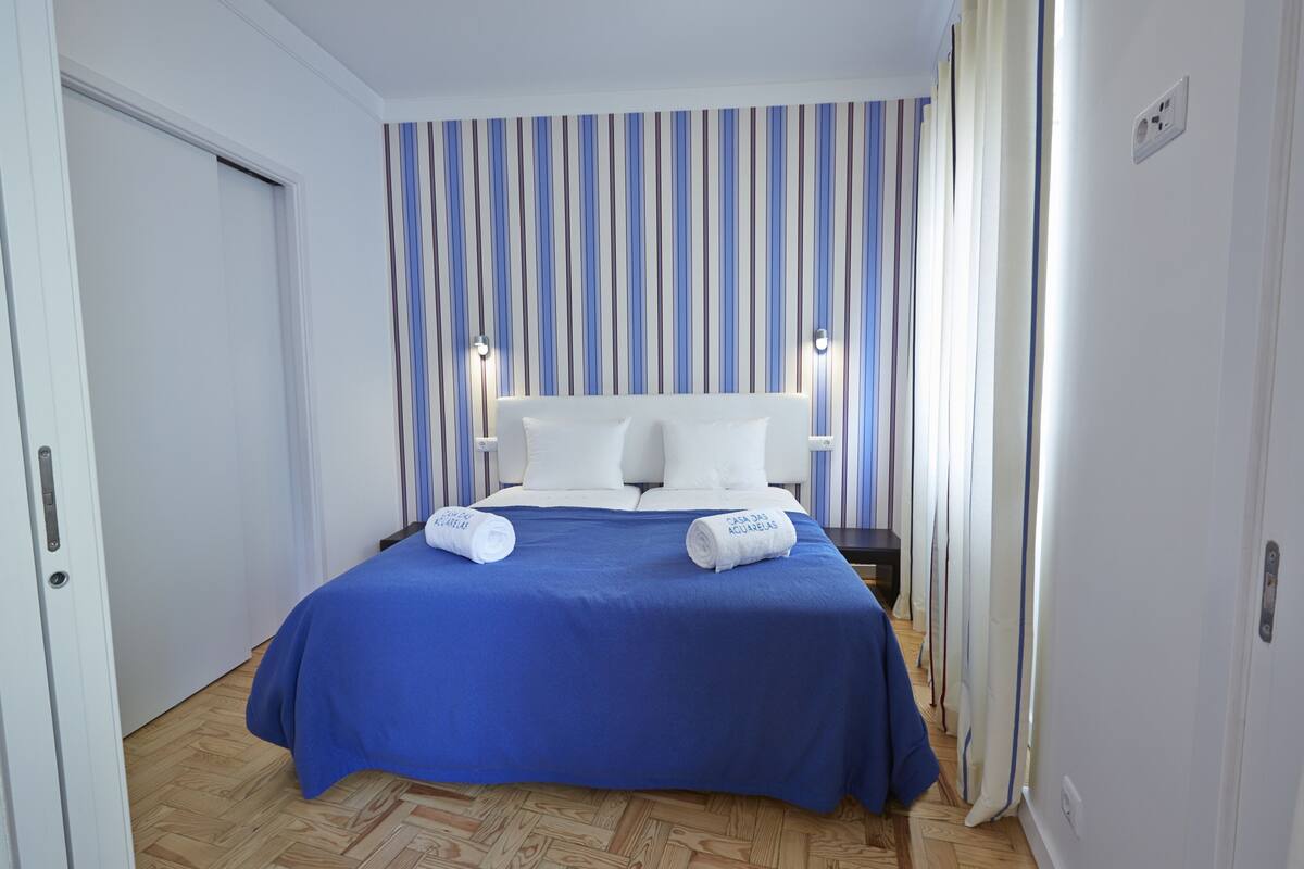 A hotel room with a large bed, striped wallpaper, and a blue bedspread.