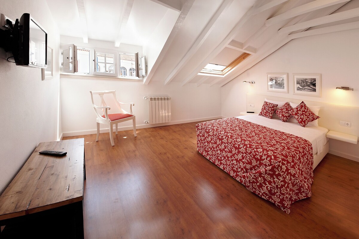 Ein Schlafzimmer mit Bett, Stuhl, Schreibtisch und Dachfenster.