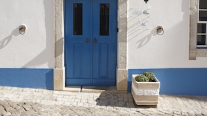 Une porte bleue avec deux fenêtres, une plante en pot et une enseigne sur le mur.