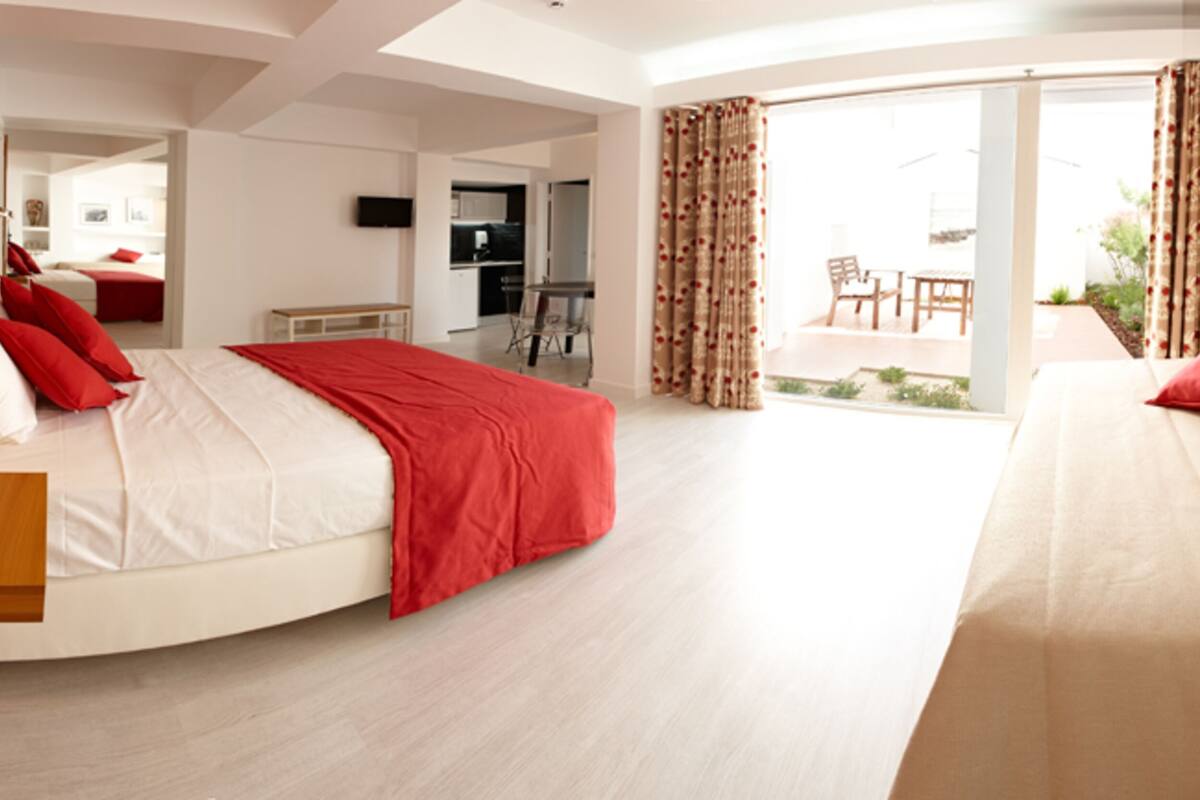 A modern hotel room with a curved bed, a separate sofa, a dining area, and a sliding glass door to the outside.