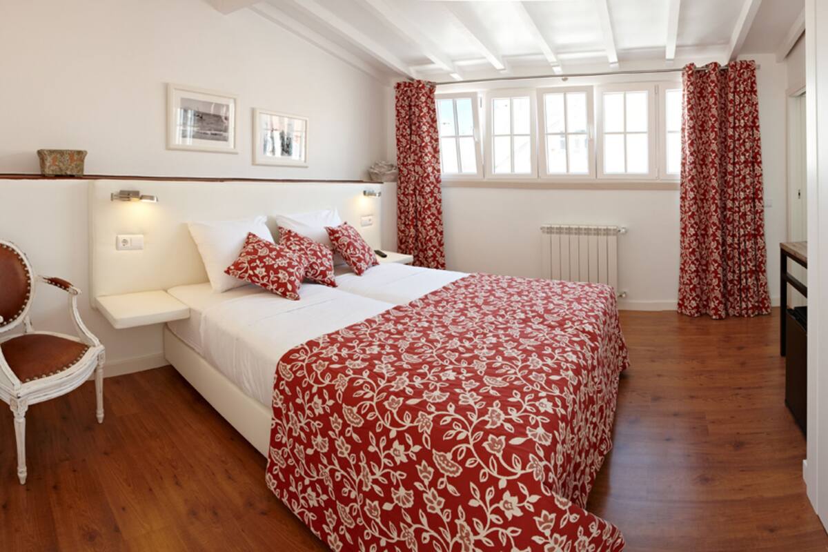 A bedroom with a large bed, a chair, a bedside table, and a window with curtains.