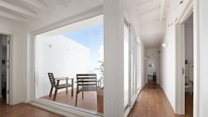 Une pièce spacieuse dotée d’une grande porte-fenêtre coulissante qui donne sur un patio extérieur avec un plancher en bois et deux chaises.