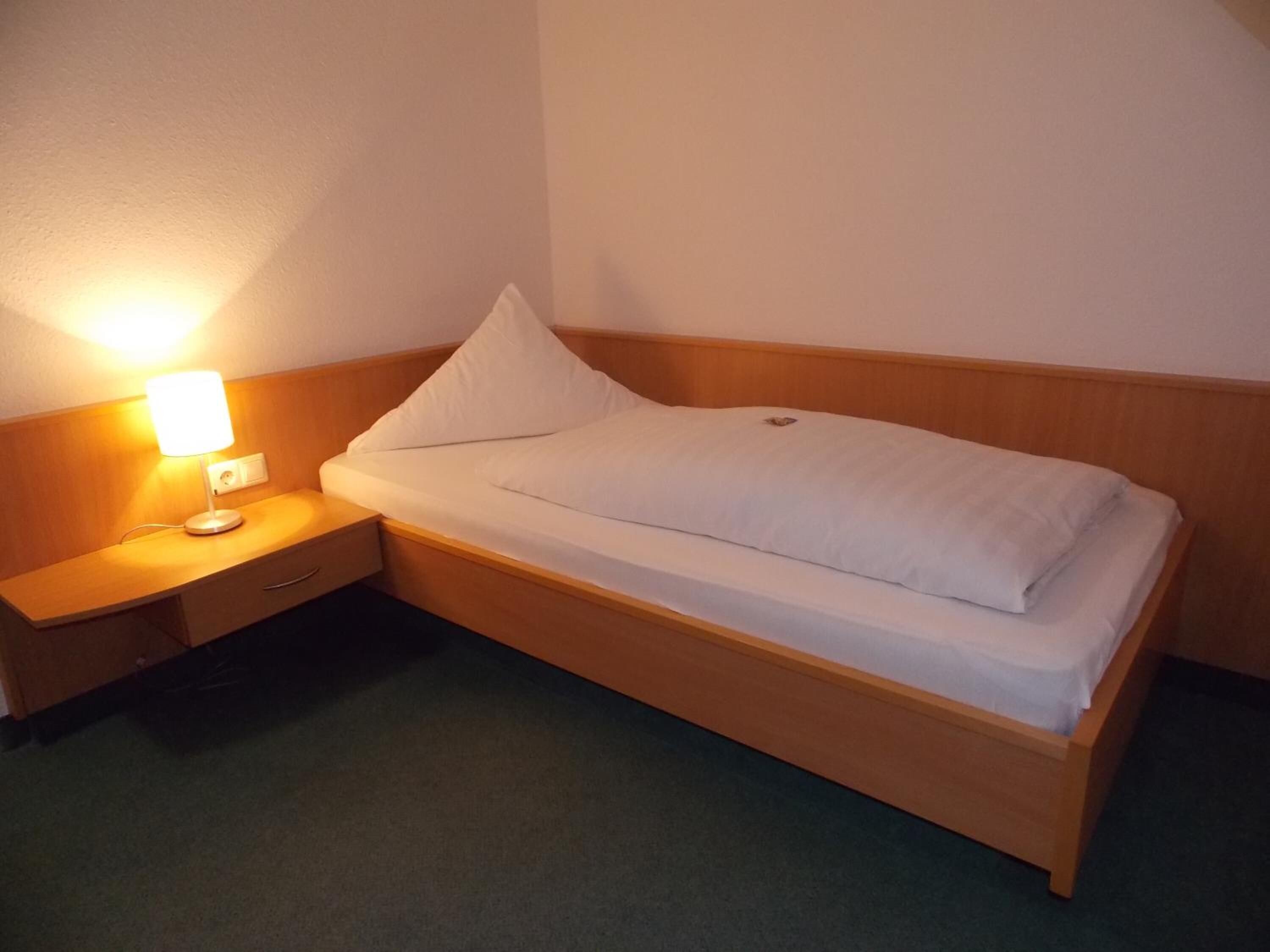 Een enkel bed met een houten hoofdbord en een nachtkastje met een lamp.