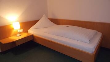 Een enkel bed met een houten hoofdbord en een nachtkastje met een lamp.