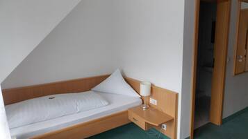 A small, single-bed room with a wooden headboard, a bedside table with a lamp, and a door leading to a bathroom.