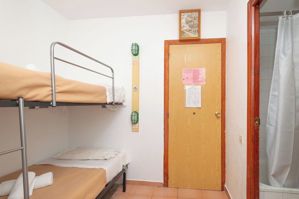Una habitación individual con una cama nido, una puerta de madera con un aviso y una cortina de ducha.