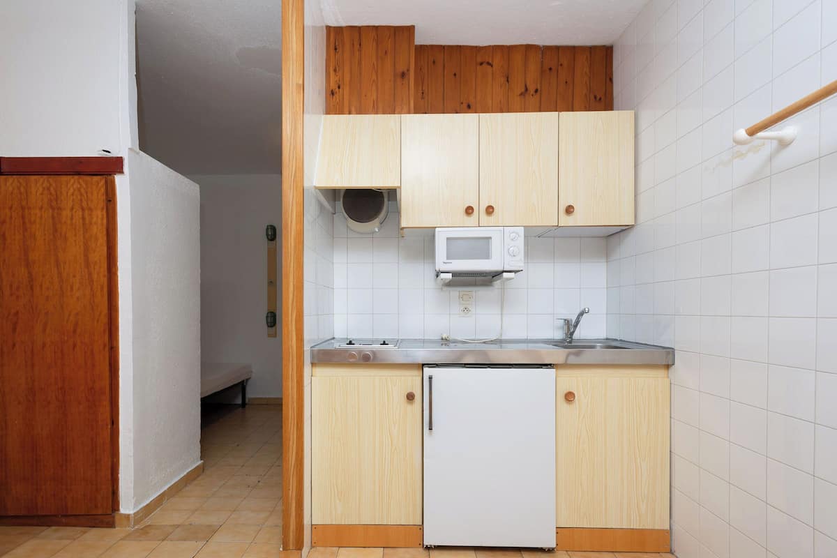 Cocina compacta con armarios de madera, microondas, pileta y un refrigerador pequeño.