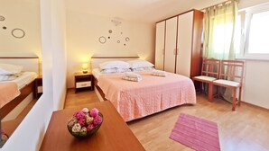 A bedroom with a bed, bedside tables, a wooden wardrobe, a chair, a table with a bowl of decorative balls, and a window with curtains. - Apartments Rooms PORAT (Split)