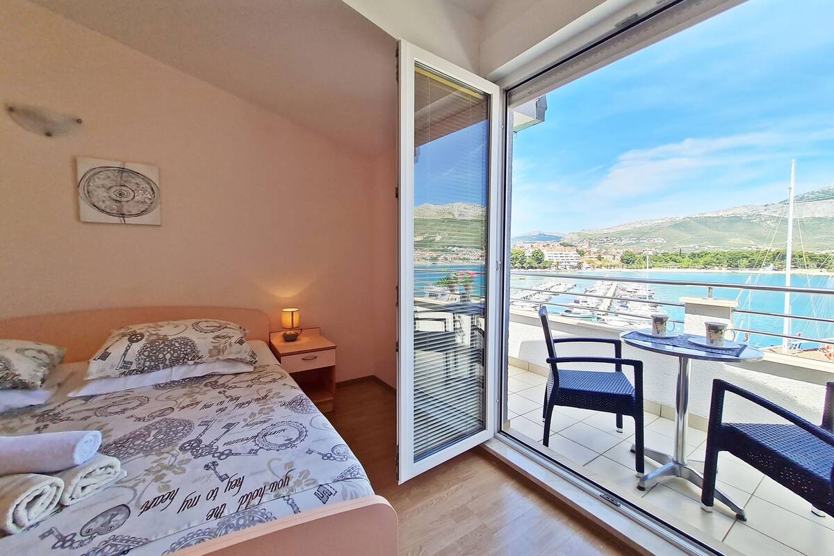 A bedroom with a bed, bedside table, and a view of a marina through a large sliding glass door.