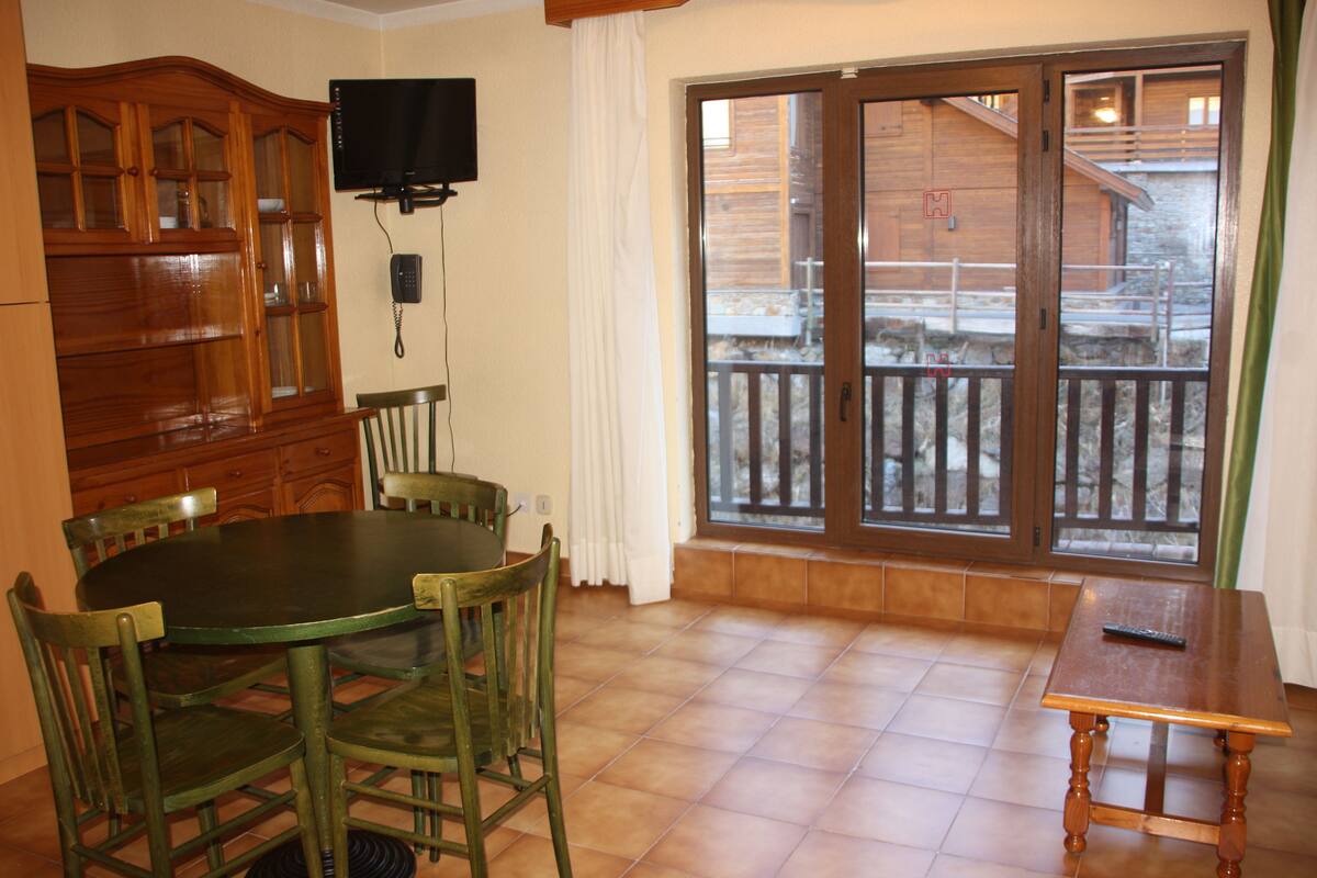 A dining area with a round table and chairs, a wooden cabinet, a television, and a sliding glass door leading to an outdoor area.