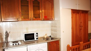 A compact kitchen with wooden cabinets, a microwave, a washing machine, and a sink. - Deusol 3000 (Soldeu)