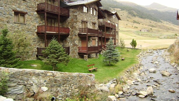 A stone building with wooden balconies and a grassy area in front. - Deusol 3000 (Soldeu)