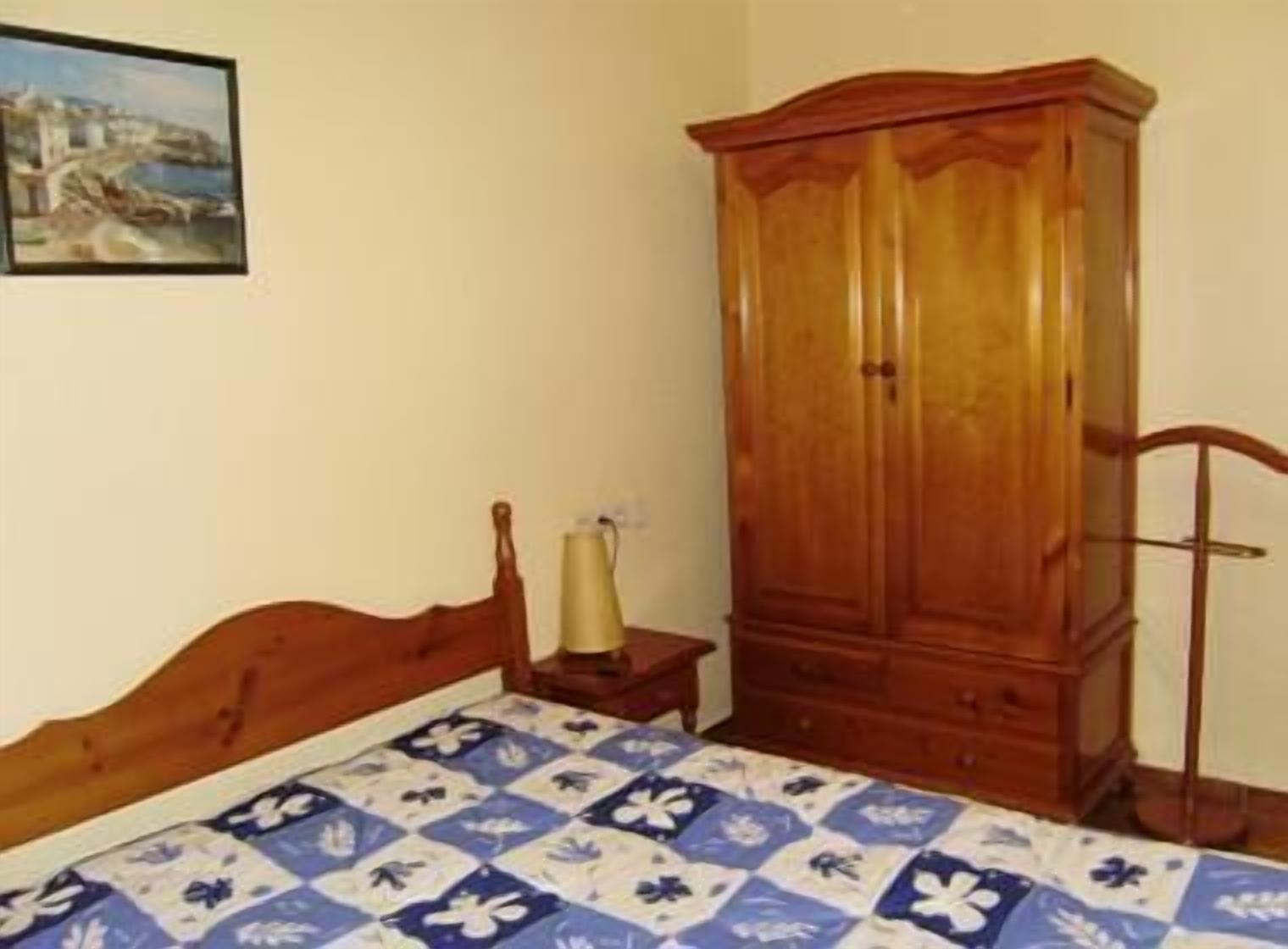 Une chambre à coucher avec un lit en bois, une armoire en bois, une petite table de chevet avec une lampe et un tableau accroché au mur.