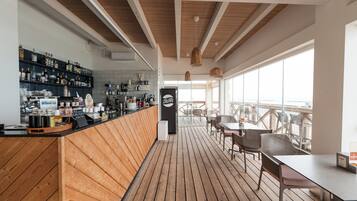 Eine Bar mit Holzboden, einer Theke voller Flaschen und Blick durch große Fenster nach draußen.