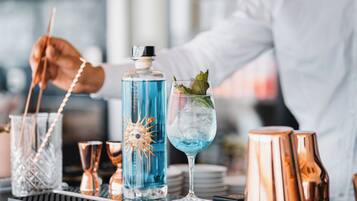 Un bancone bar con un barista che prepara un cocktail, una bottiglia di liquido blu e shaker per cocktail in rame.