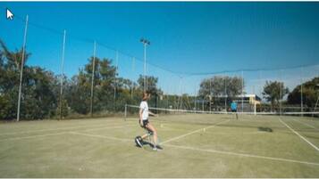 A tennis court with a net, surrounded by a fence and trees.
