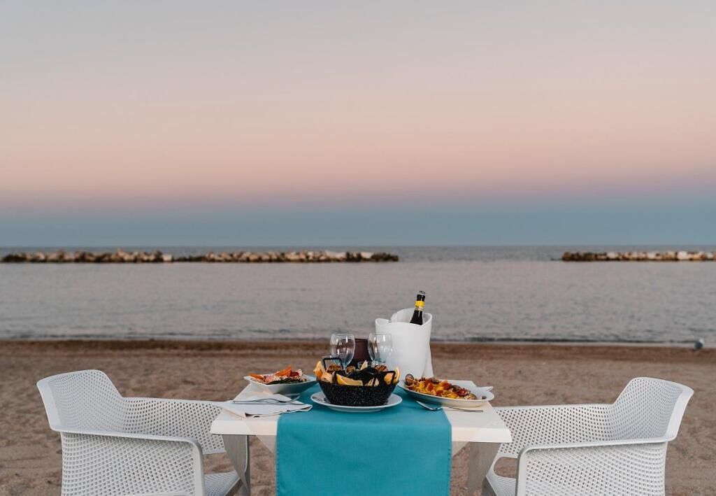 Une table dressée pour deux personnes, avec vue sur la mer au coucher du soleil.