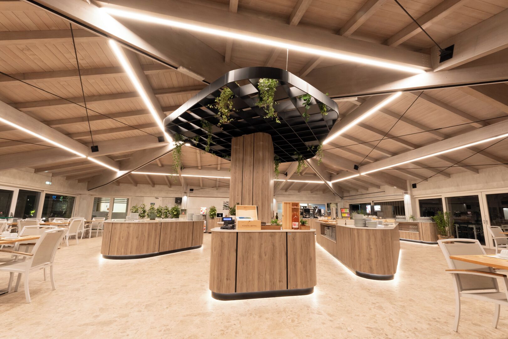 A spacious, modern interior with high ceilings, wooden reception desks, and a central column with greenery.