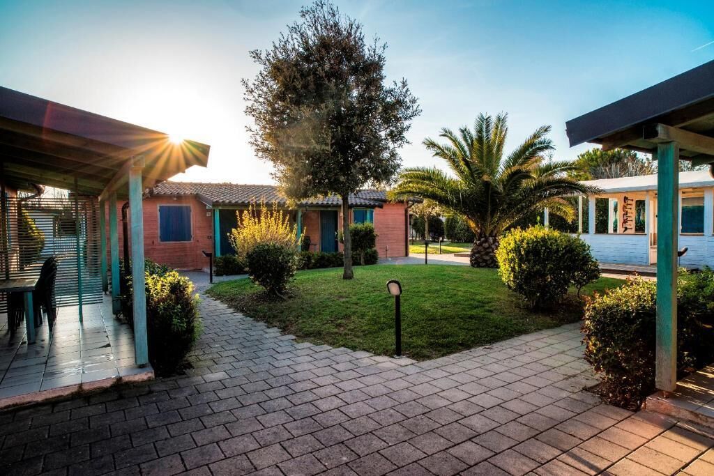 A courtyard with a paved walkway, a covered seating area, and a building with a tiled roof.