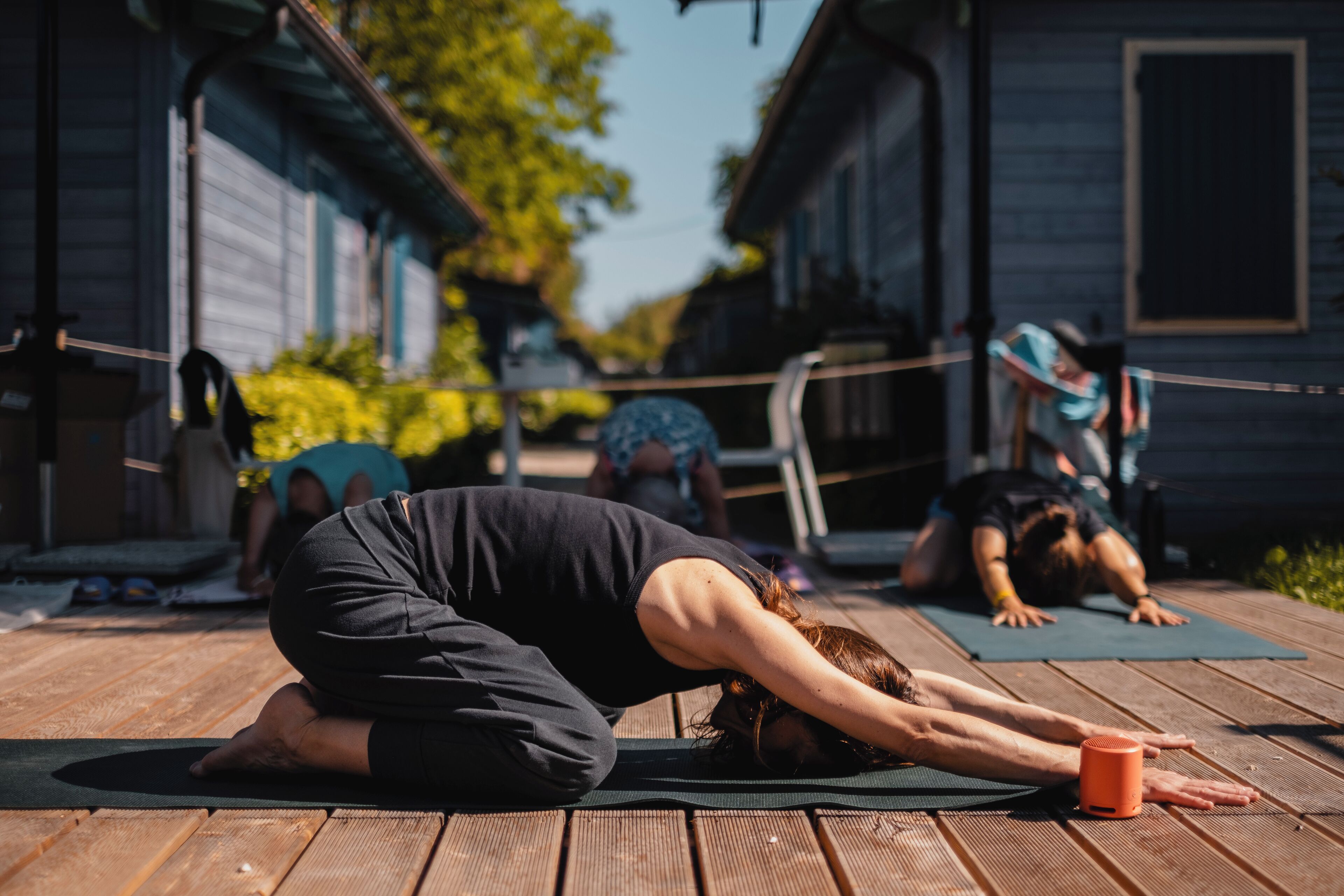 A wooden deck with yoga mats and a person in a forward bend pose.