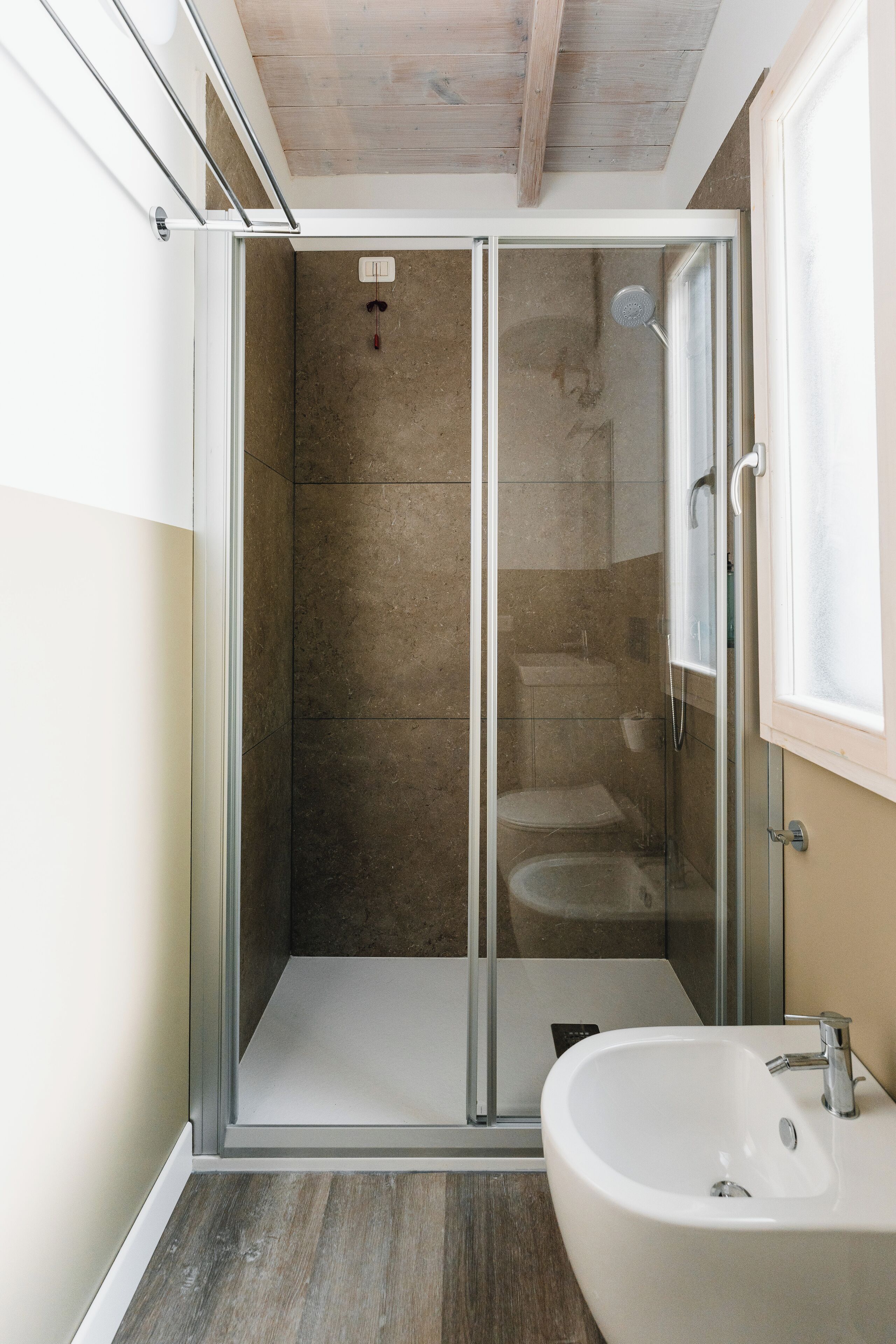 Een moderne badkamer met een glazen douchecabine, een witte wastafel en een houten plafond.