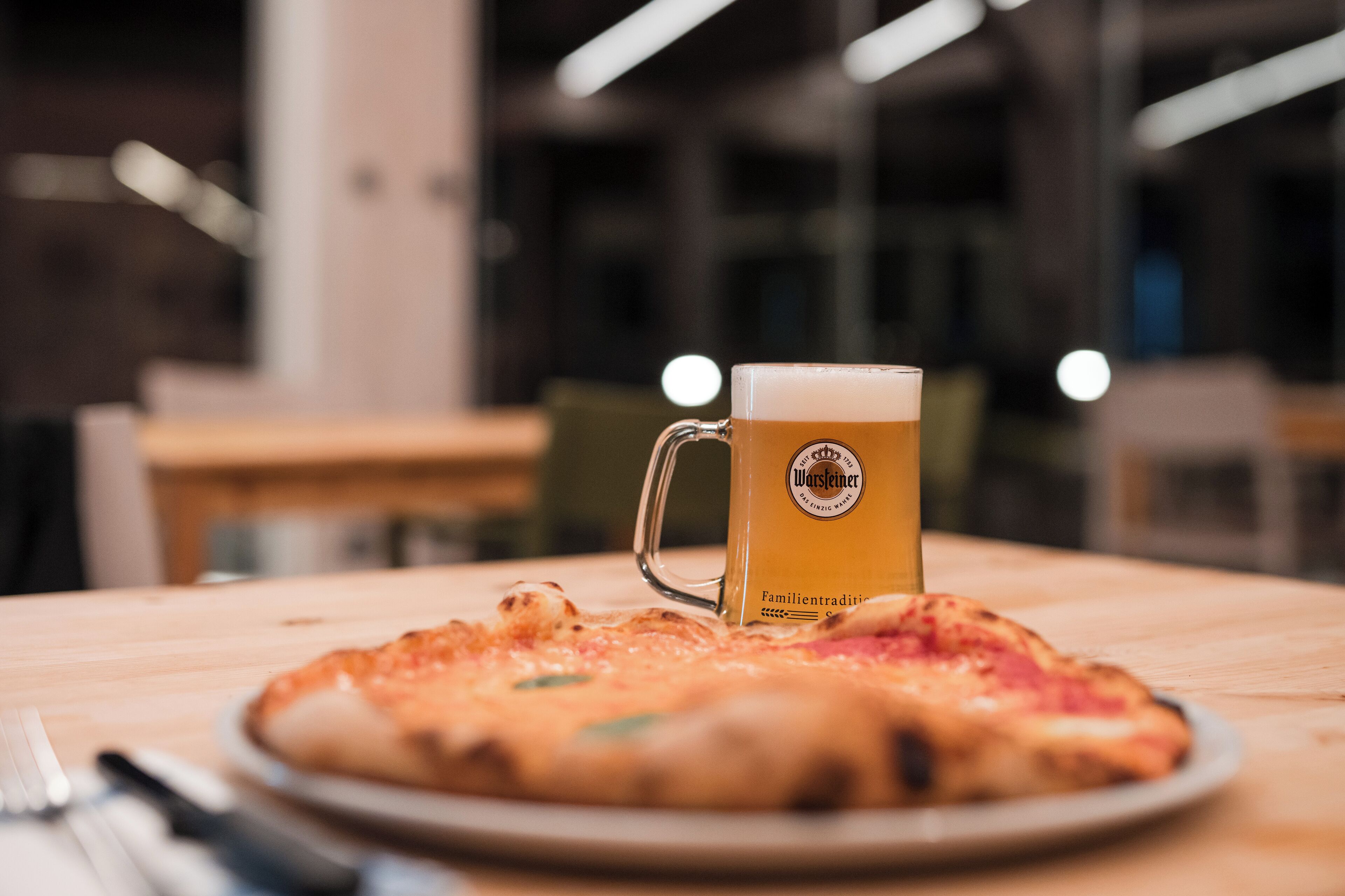 Pizza på et træbord med et ølmug glas ved siden af.
