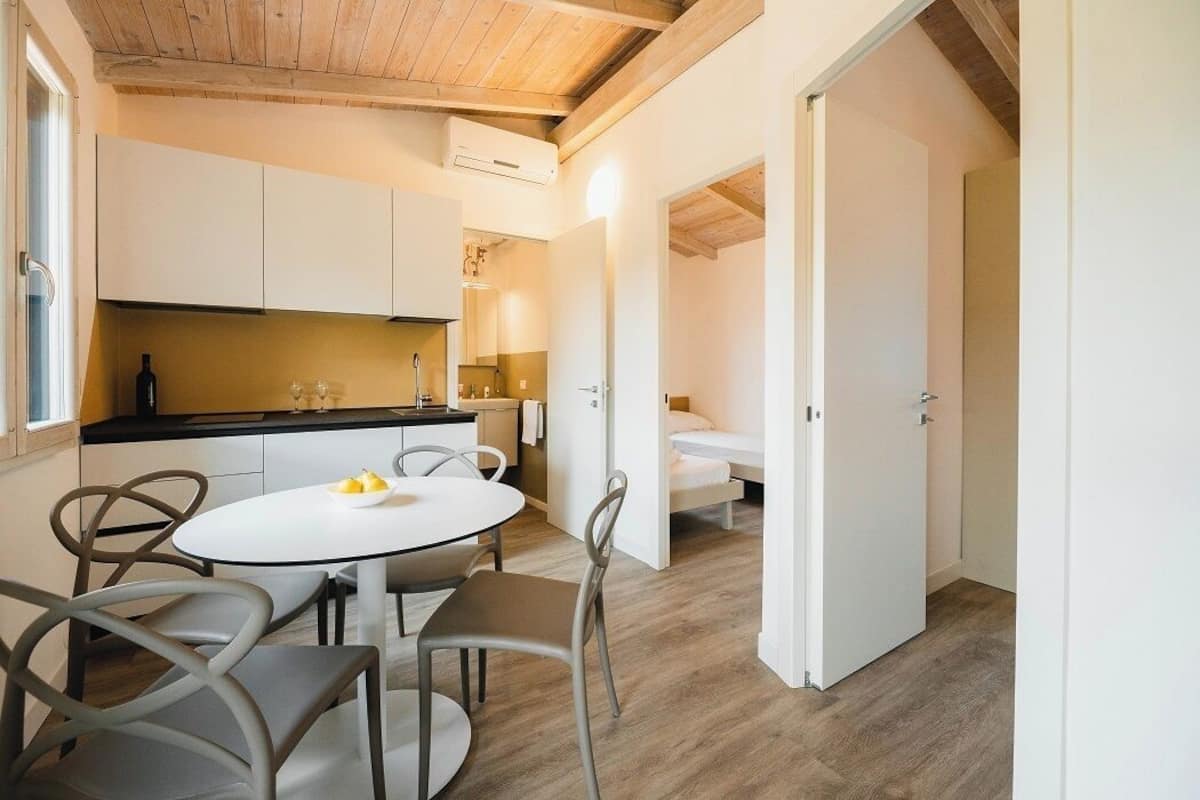 A compact kitchen with white cabinets, a round dining table, and a wooden ceiling.