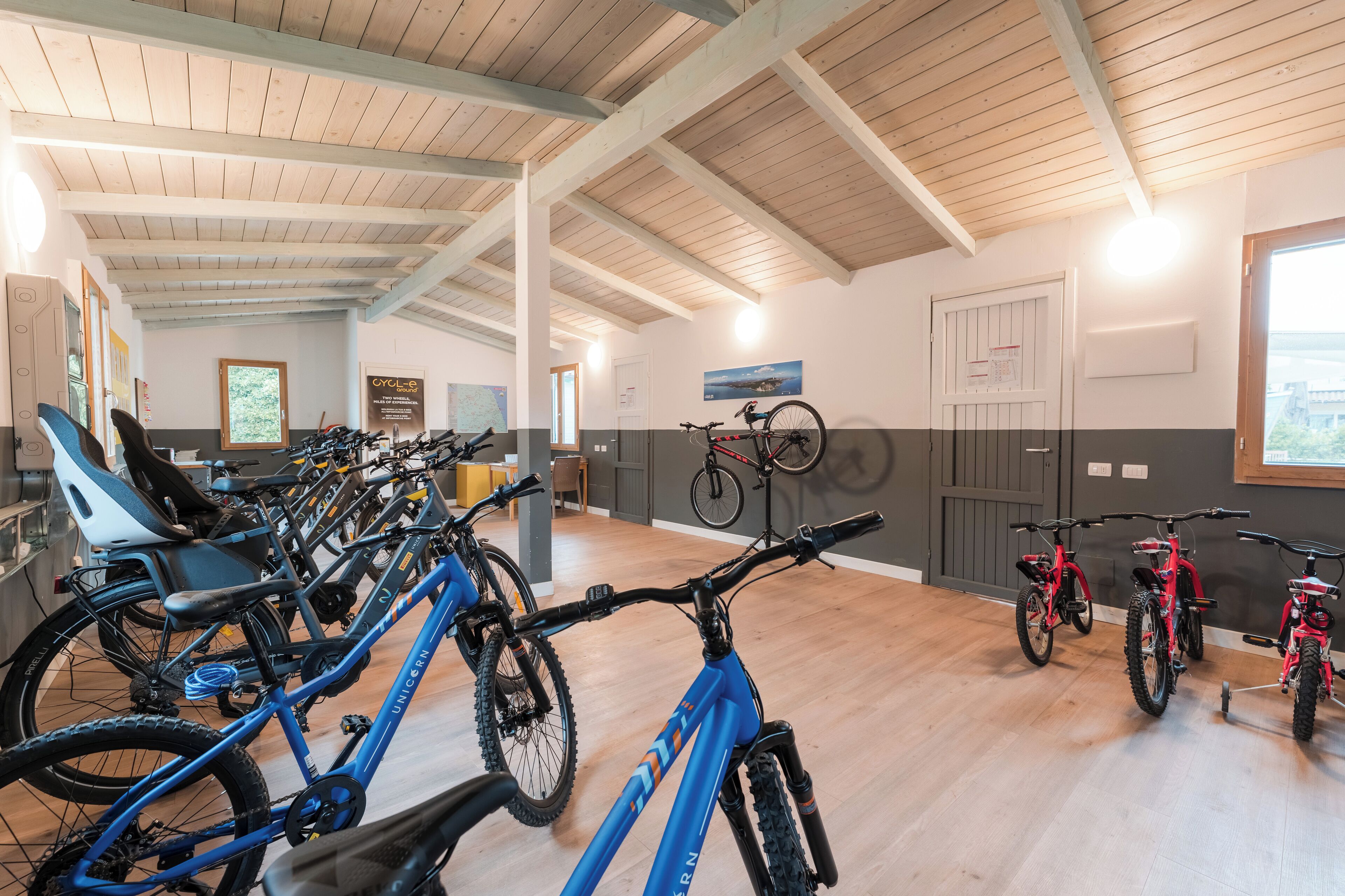 Un vaste espace intérieur doté de planchers en bois et de hauts plafonds, où l’on trouve une rangée de vélos et un fauteuil roulant.