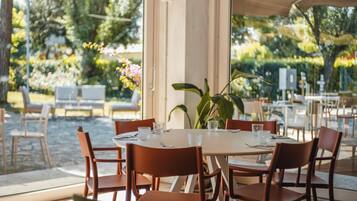 Zona pranzo all'aperto con tavolo apparecchiato per due, circondato da sedie, affacciata su piante e fiori attraverso il vetro.
