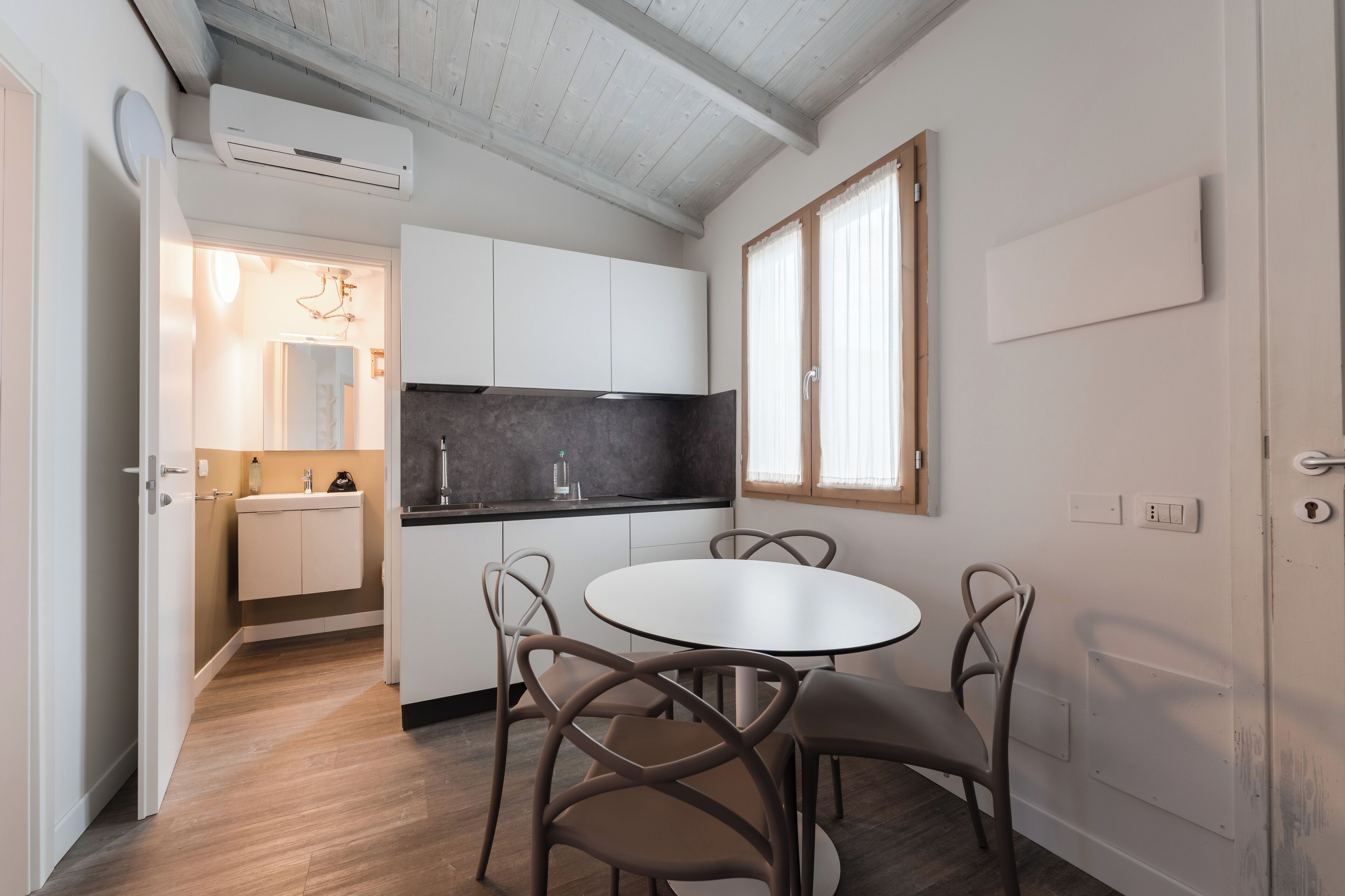 A compact kitchen with white cabinets, a black countertop, and a round dining table with four chairs.