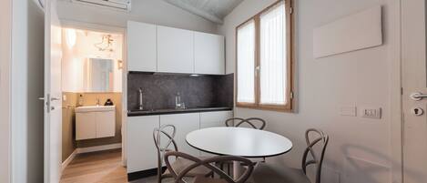 A compact kitchen with white cabinets, a black countertop, and a round dining table with four chairs.