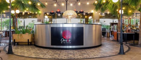 A bistro with a central counter, palm trees, and string lights.