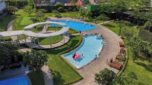 A large outdoor swimming pool with a circular water slide, surrounded by well-maintained lawns and trees. - Aston Cirebon Hotel & Convention Center (West Cirebon)