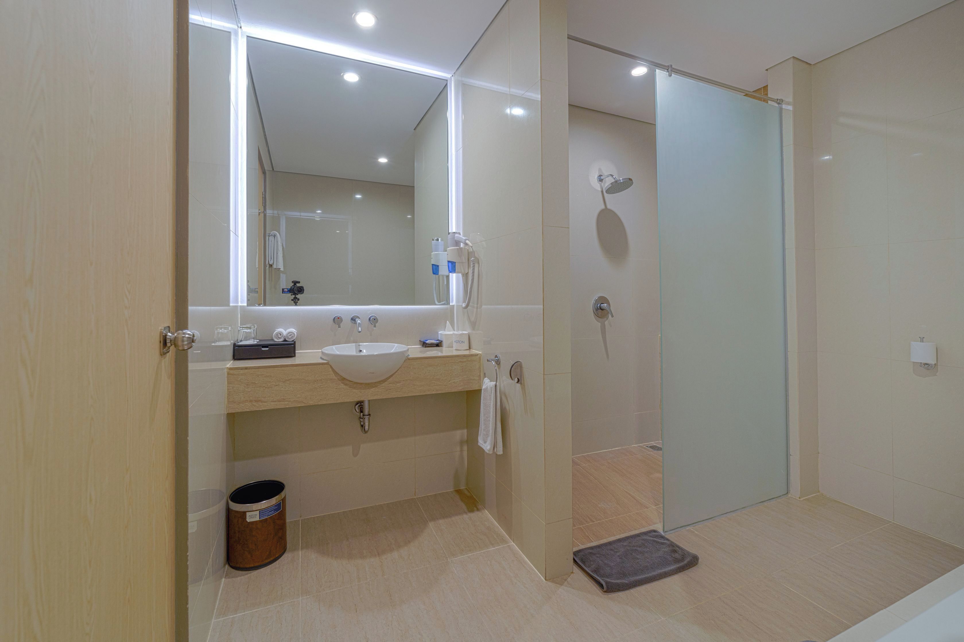 A modern bathroom with a large mirror, a sink, a shower, and a toilet.