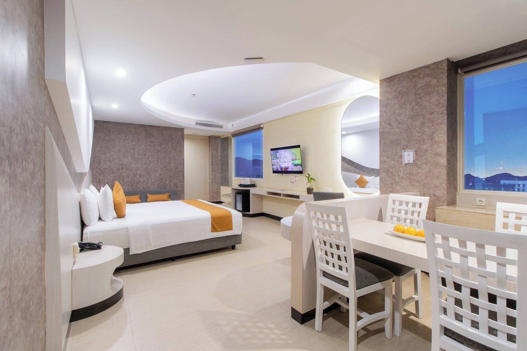 A hotel room with a bed, a desk, a chair, a TV, and a view of the cityscape.