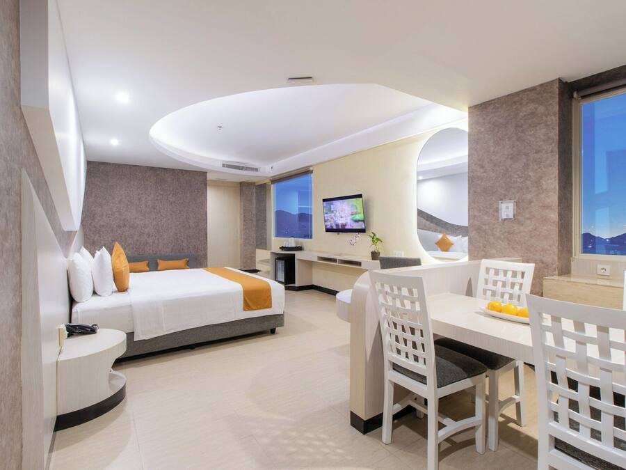 A hotel room with a bed, a desk, a chair, a TV, and a view of the cityscape.