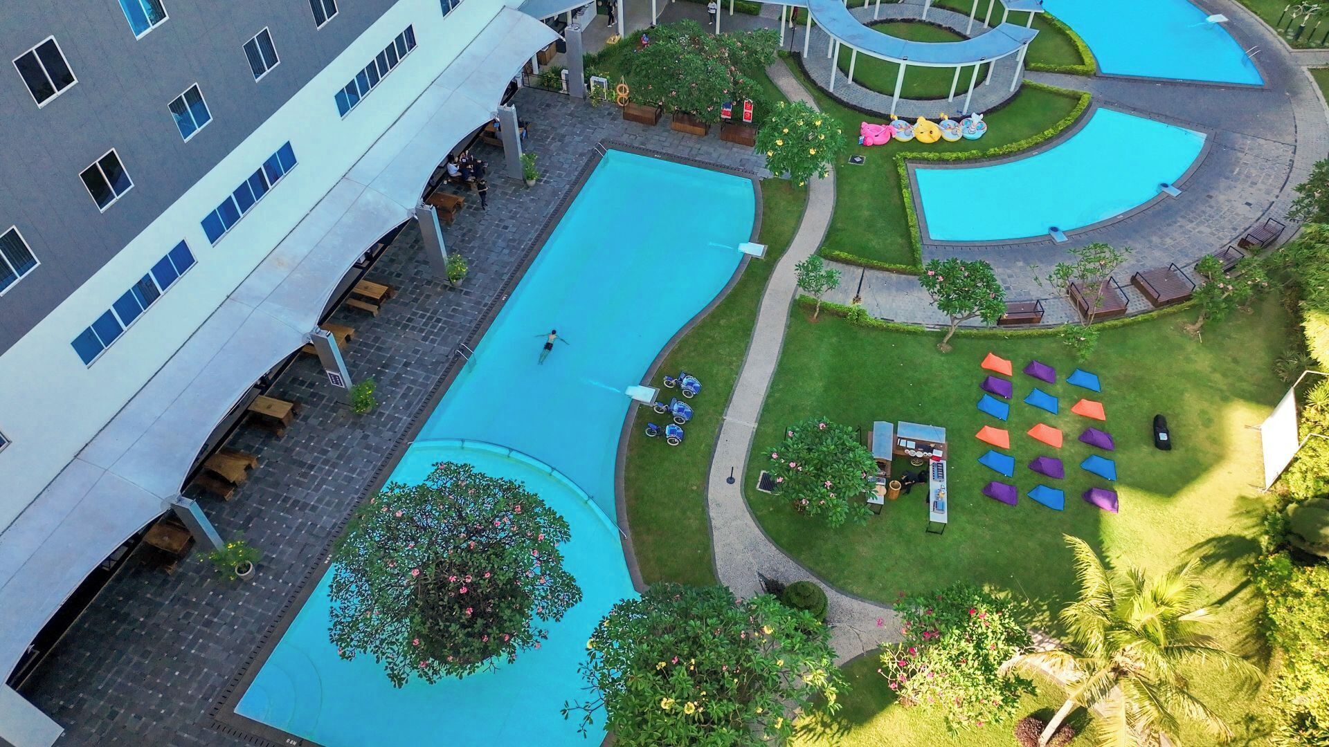 A hotel with multiple swimming pools, outdoor seating areas, and a well-maintained garden.