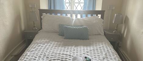 A neatly made bed with a white duvet and two pillows, a window with blue curtains, and two bedside lamps.