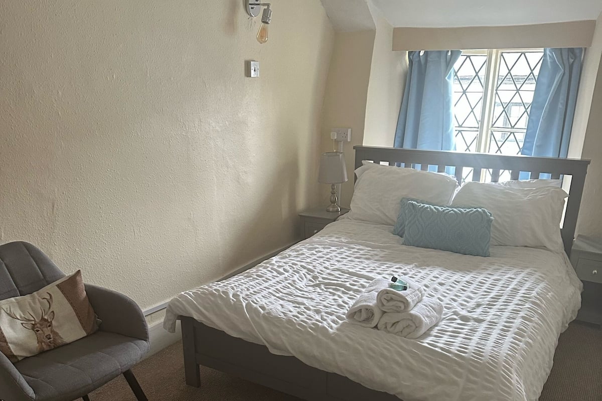 A bedroom with a bed, a chair, a lamp, and a window with curtains.
