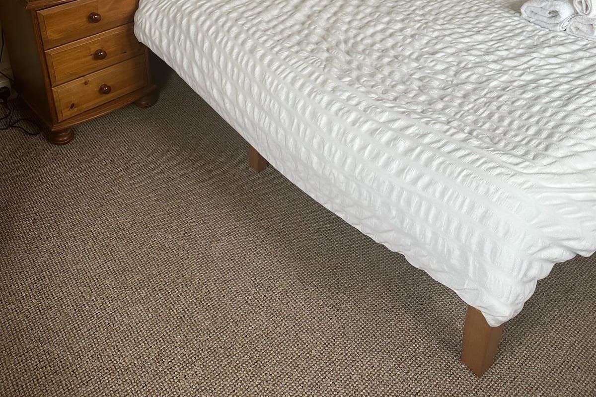 A neatly made bed with a wooden headboard, two bedside tables with lamps, and a carpeted floor.