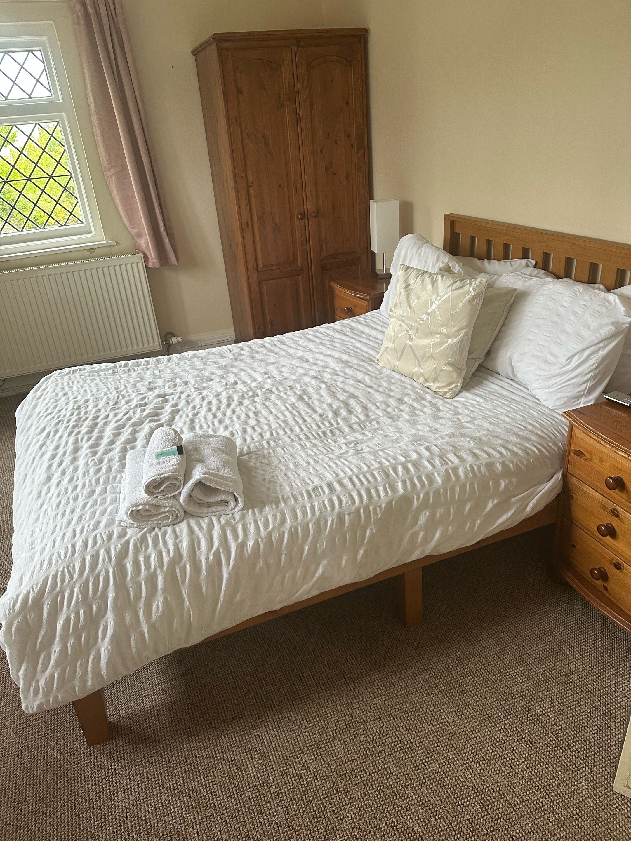 A neatly made bed with a white quilt, two pillows, and folded towels on the foot of the bed.