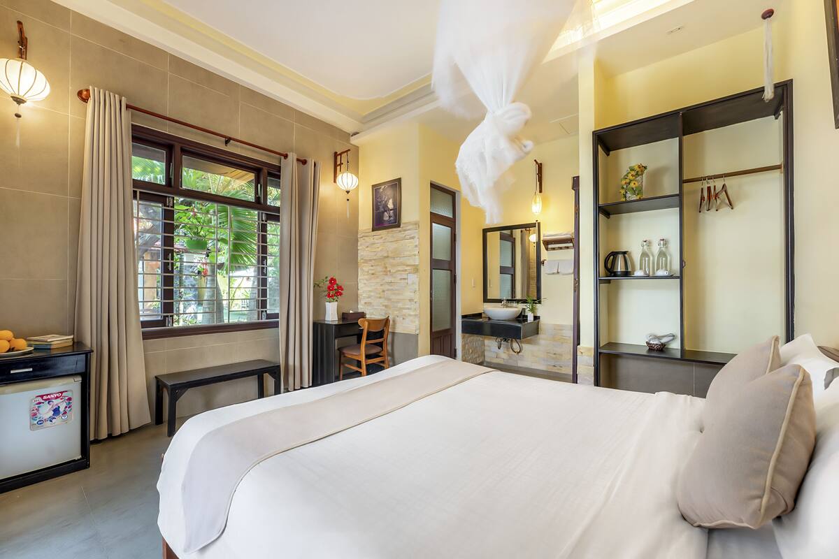 A hotel room with a large bed, a desk, a chair, a vanity with a mirror, and a shelf with toiletries.