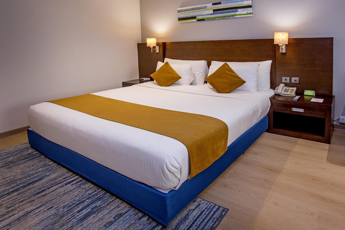 A hotel room with a large bed, a wooden headboard, bedside lamps, a telephone, and a nightstand.