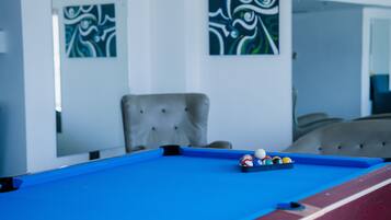 Enjoy a game of pool in this stylish room, featuring a blue table with red border and a tufted armchair.