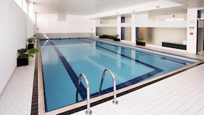 Una amplia piscina interior con agua cristalina y paredes y suelos de baldosas blancas.