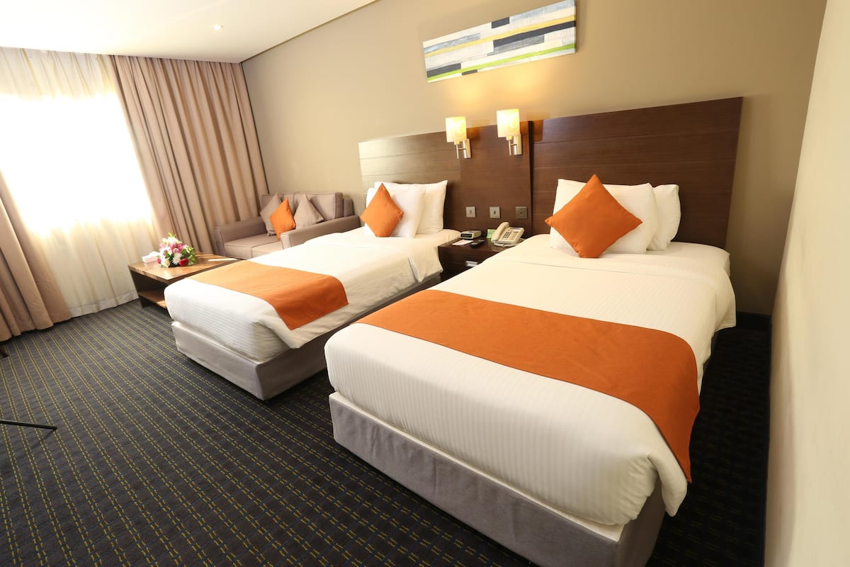 A hotel room with two beds, a sofa, a nightstand, and a window with curtains.