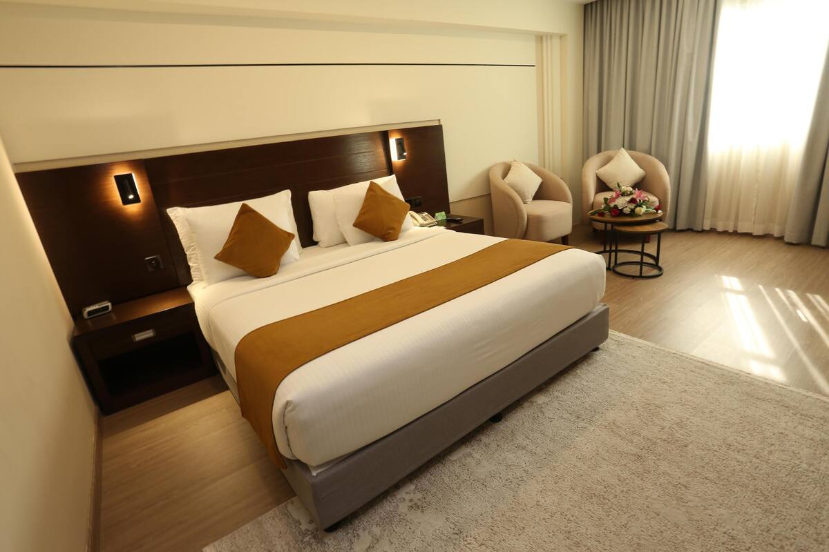 A hotel room with a large bed, a nightstand, a chair, and a small table with flowers.