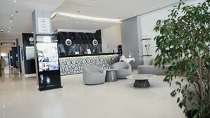 Un lobby moderno con un mostrador de recepción, zona de estar y una planta en maceta grande.